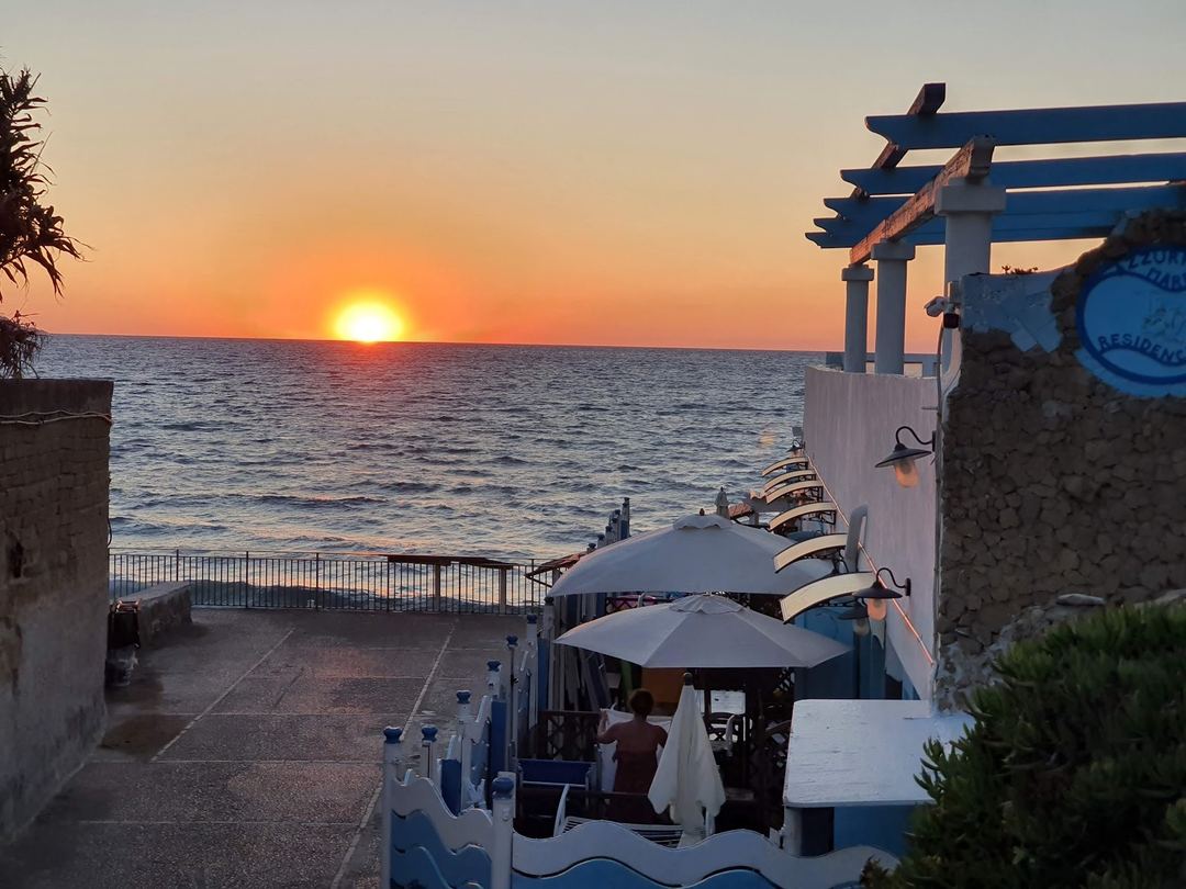 Sunset view over the Mediterranean Sea from the Azzurromare Residence's seaside terrace with shaded dining area.