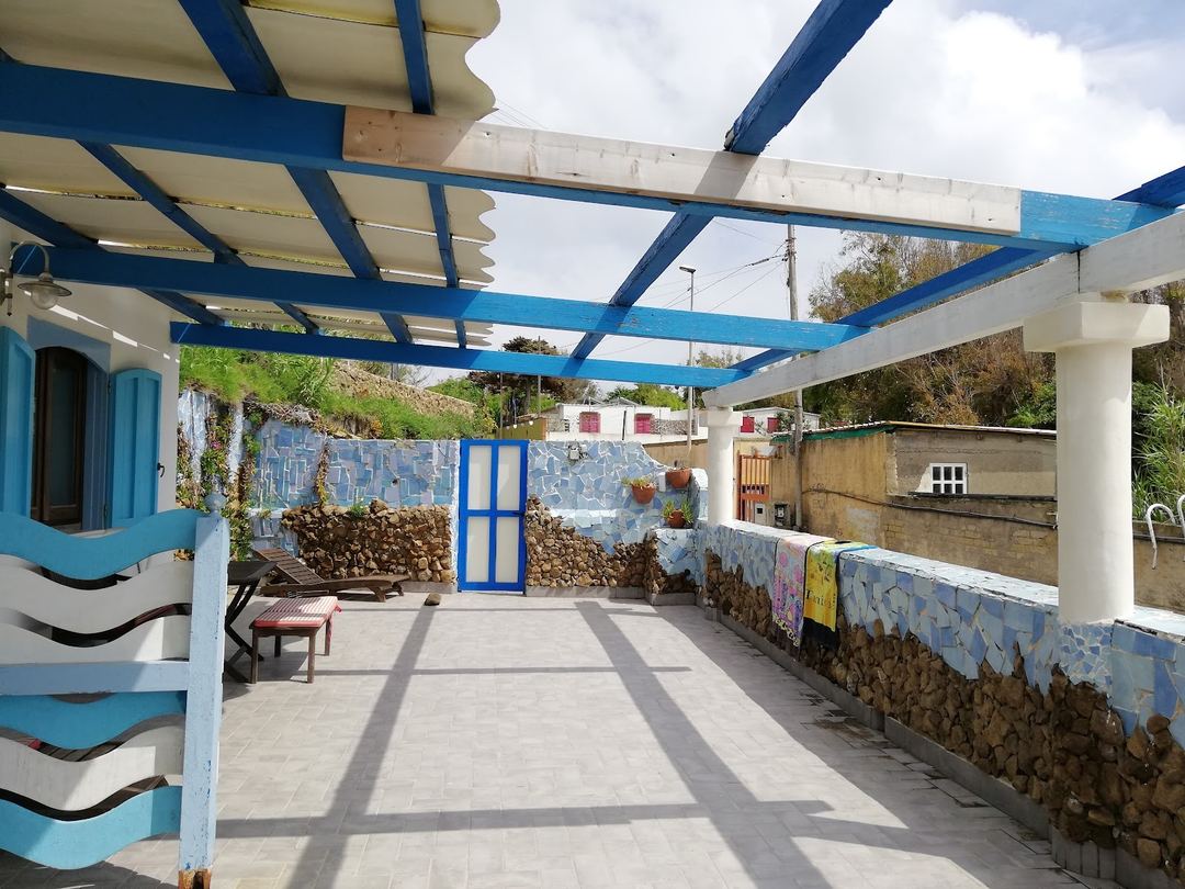 A bright courtyard terrace with blue and white pergola overhead, stone walls, and rustic Mediterranean architecture at Azzurromare Residence.