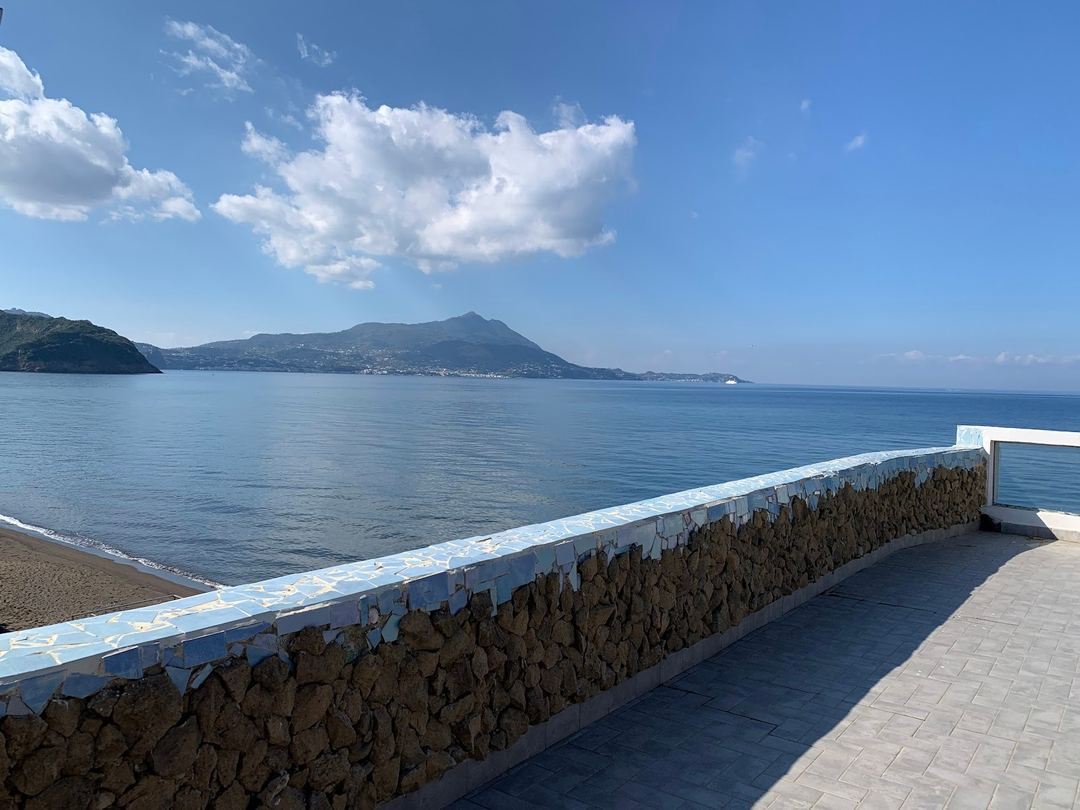 Panoramic sea view from the property's terrace overlooking a volcanic mountain across the bay under clear blue skies.